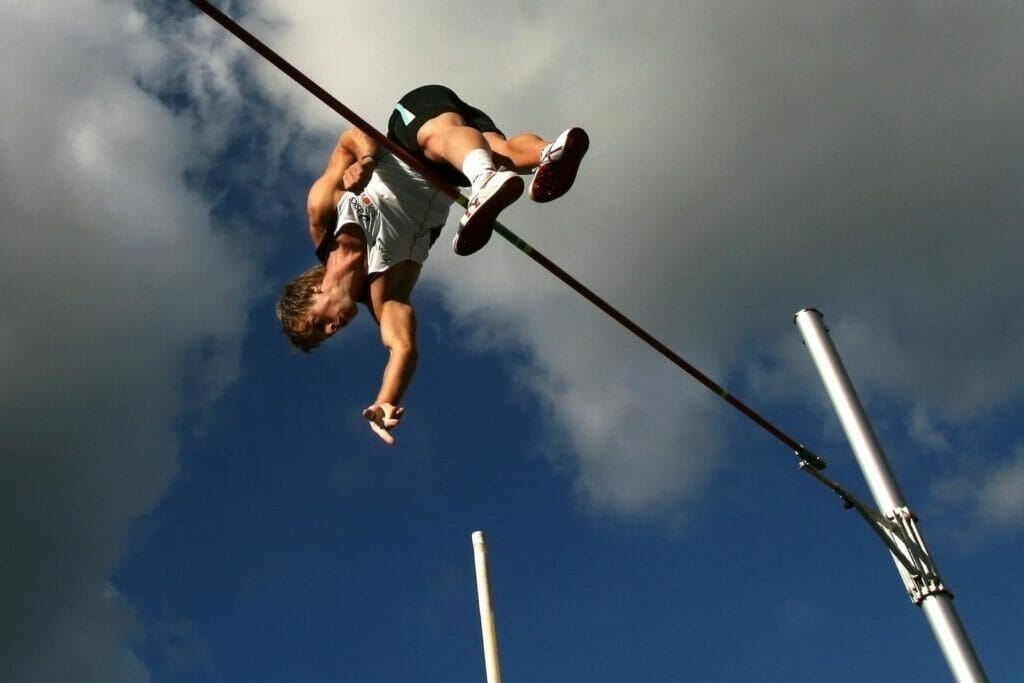 man in white tank top and black shorts hanging on black metal bar under blue sky